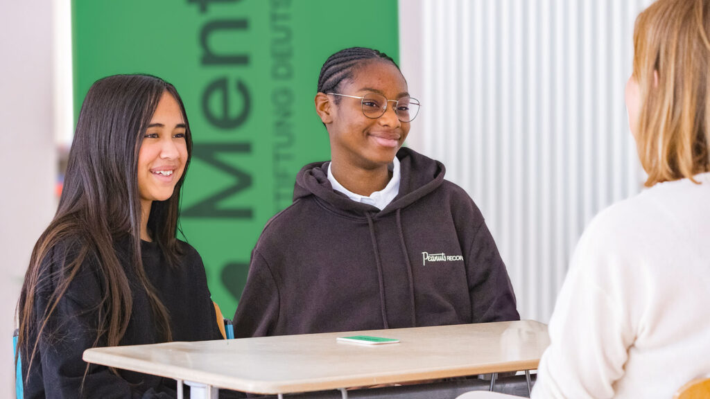 Zwei Schülerinnen sprechen mit einer Mentorin im Klassenzimmer