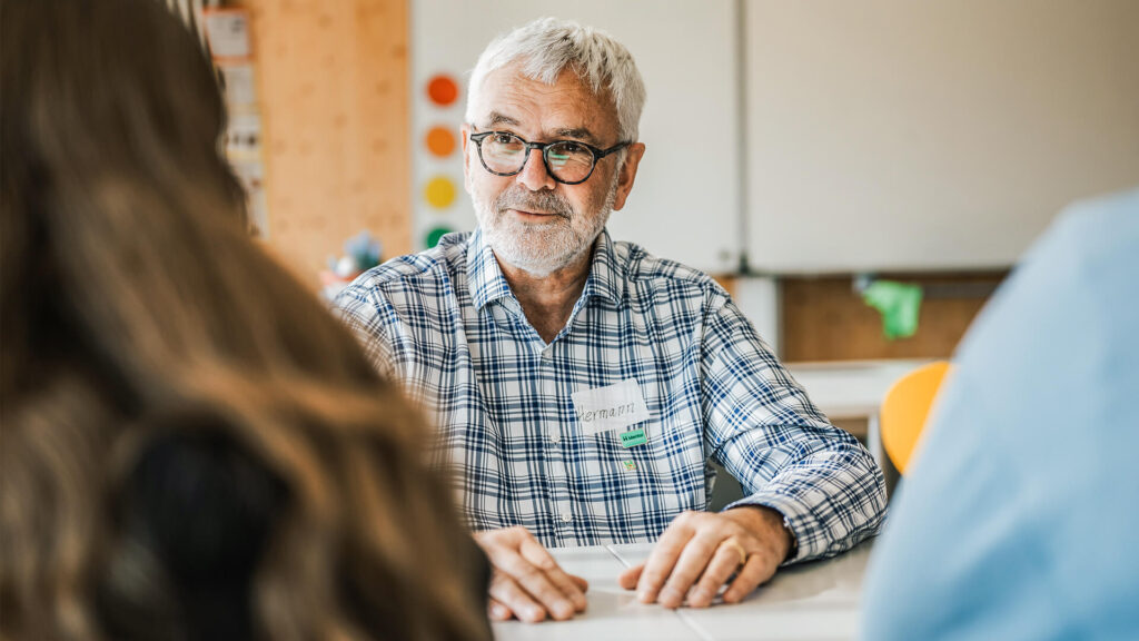 Ein Mentor spricht mit Schülerinnen im Klassenzimmer