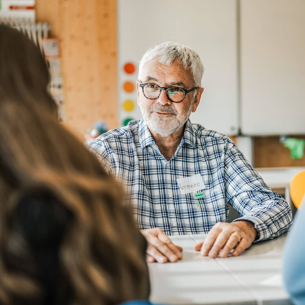 Mentor hört interessiert einer Schülerin im Gespräch zu.