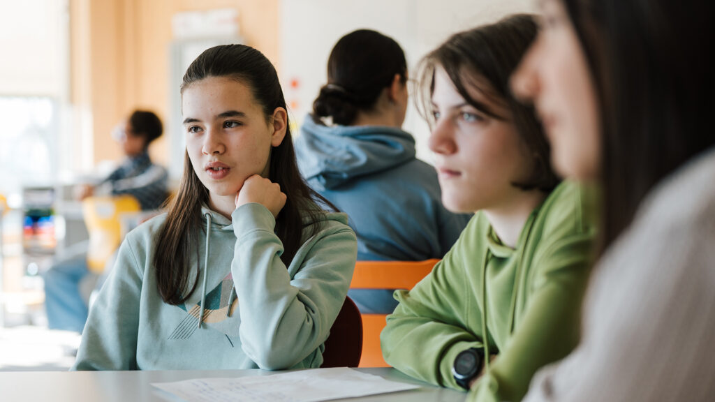 Jugendliche Mädchen sitzen an einem Tisch in der Schule und sprechen miteinander