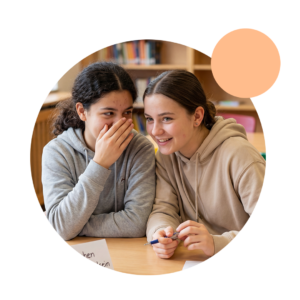 Zwei Jugendliche Mädchen sitzen im Unterrricht und flüstern sich etwas zu